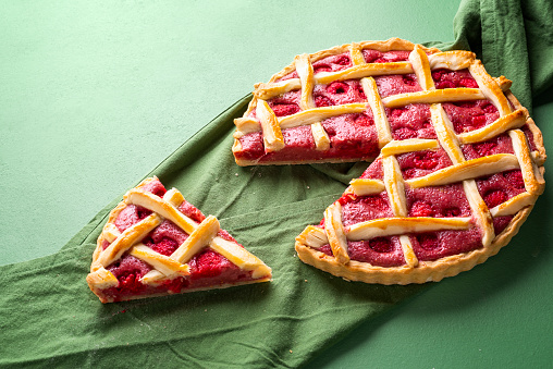 Tasty raspberry pie with lattice crust and one slice on a green napkin. Classic dessert. Summer cake. Easiest pie. Raspberry tart with a pastry crust