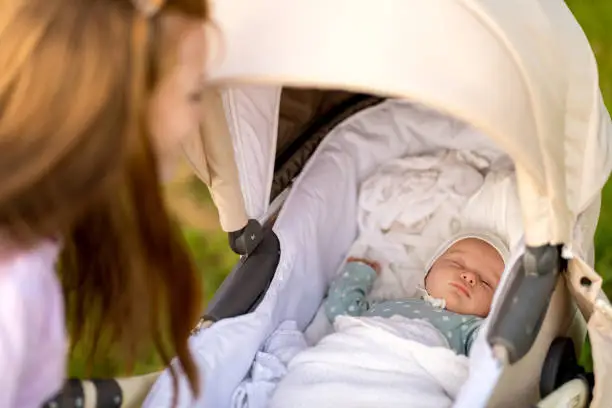 Newborn baby sleeps lying in a stroller on a walk with mom
