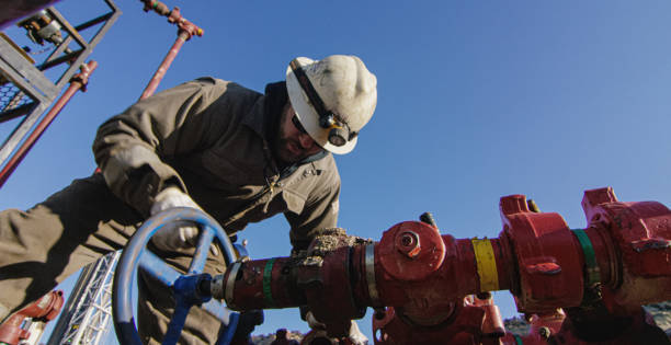 An Oilfield Worker in His Thirties Pumps Down Lines at an Oil and Gas Drilling Pad Site on a Cold, Sunny, Winter Morning An Oilfield Worker in His Thirties Pumps Down Lines at an Oil and Gas Drilling Pad Site on a Cold, Sunny, Winter Morning oil wellhead stock pictures, royalty-free photos & images