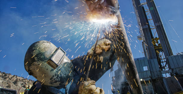 An Oilfield Worker Welds an End Cap to a Pipe as Sparks Fly Next to a Derrick at an Oil and Gas Drilling Pad Site on a Sunny Day An Oilfield Worker Welds an End Cap to a Pipe as Sparks Fly Next to a Derrick at an Oil and Gas Drilling Pad Site on a Sunny Day automatic welding torch stock pictures, royalty-free photos & images
