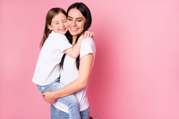 美しい若い母親の写真は腕を保持小さな娘2人の女性が親友の素敵な感情の目を抱きしめるカジュアルなtシャツジーンズを着て、パステルピンクの色の背景を分離 - clothing love smiling parent ストックフォトと画像