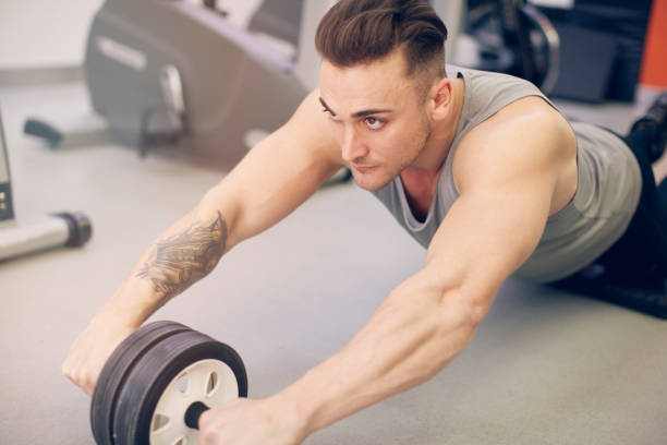 istock Young man working out at gym with abs wheel 1222082452