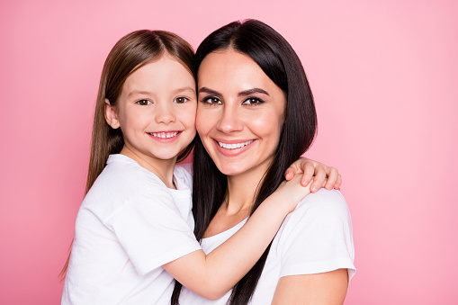 Closeup photo of beautiful young mother hold arms little daughter, hugging best friends sincere cardiac feelings wear casual white t-shirts isolated pastel pink color background