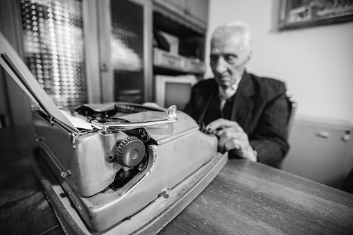 Senior Caucasian man writing on old typewriter at home during lockdown.