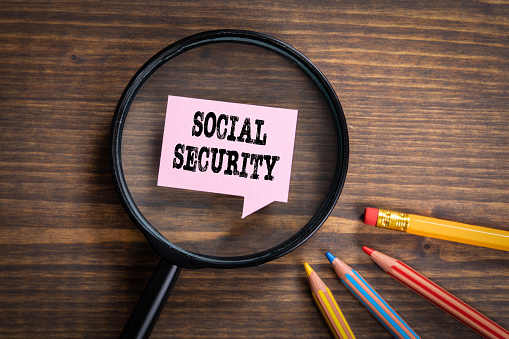 SOCIAL SECURITY. Black magnifying glass, speech bubble and colored pencils on a wooden background