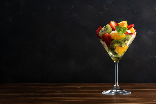 Fruit cocktail in martini glass on wooden table. Food vegan concept.