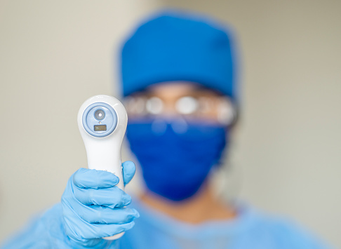 Ethnic medical professional holding up a non-contact thermometer to check patients temperature.