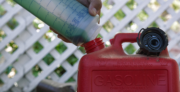 Close-Up Shot of a Hispanic Man's Hands Pouring Outboard Motor Oil from a Plastic Measuring Cup into a Red, Plastic Gasoline Can Outdoors