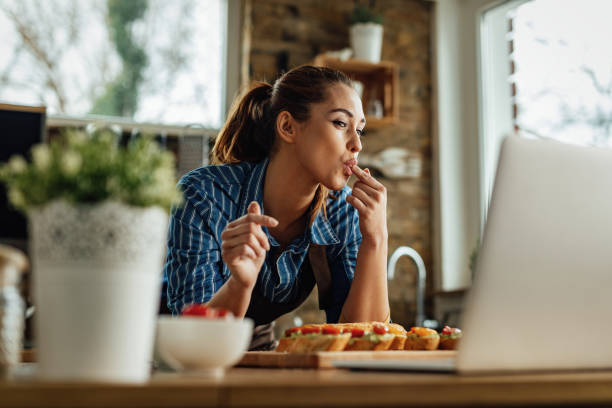 istock Happy woman blogging over laptop while making bruschetta in the kitchen. 1222086587