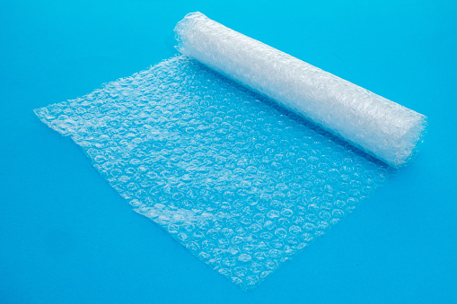 Clear plastic bubble wrap packaging stretched out over a plain blue background - studio shot