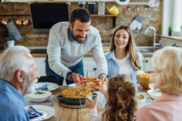 istock Happy man serving appetizer to his family while having lunch in dining room. 1222087997