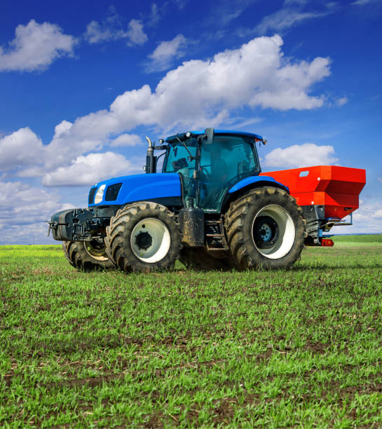 istock blue tractor in field work with modern red two-disc fertiliser spreader sprayer. Agrarians feeding winter crops, disk spreaders of winter crops 1222088161