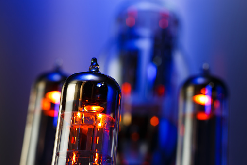 Vacuum electronic radio tube close-up. Glowing orange on dark blue background.