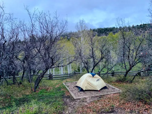 A Pitched Tent Stands in a Camping Spot in a Fenced-In Campground near a Hillside and a Forest in Western Colorado