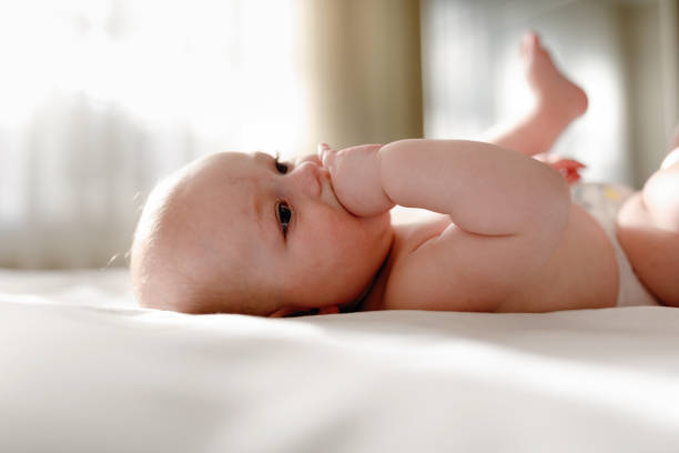 istock Adorable barefoot child in diaper smiling while playing on white bedding 1222092313