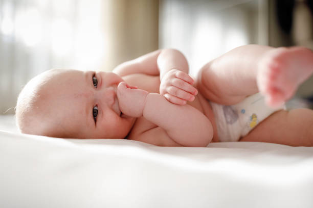 istock Adorable barefoot child in diaper smiling while playing on white bedding 1222093346