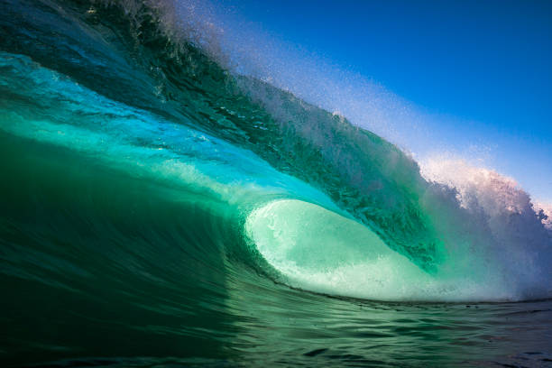 Emerald green wave crashing in ocean with blue sky