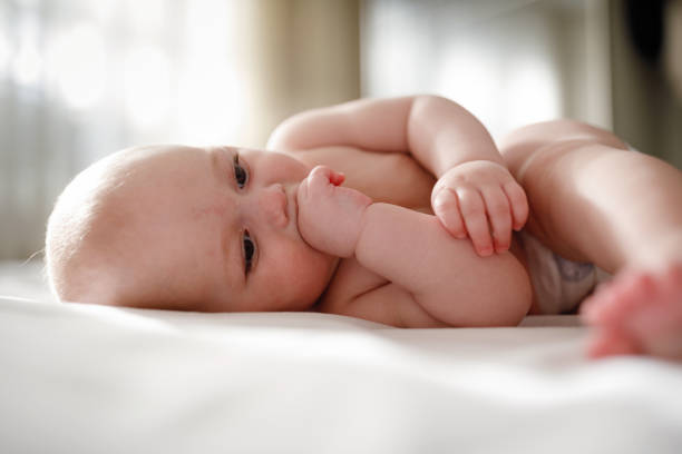 istock Adorable barefoot child in diaper smiling while playing on white bedding 1222095149