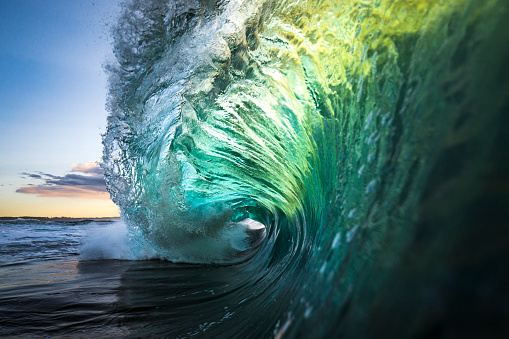 Large colourful wave breaking in ocean over reef and rock