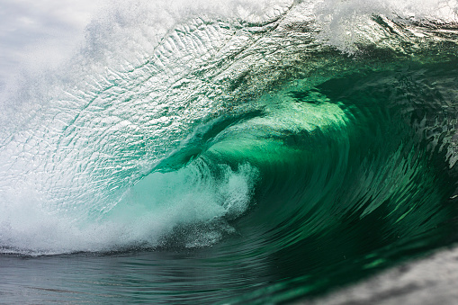 A powerful emerald green wave breaking in the ocean against a stormy backdrop, photographed in the morning out in the ocean.