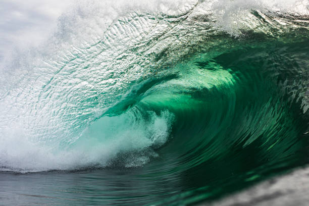 Emerald green wave breaking in the ocean A powerful emerald green wave breaking in the ocean against a stormy backdrop, photographed in the morning out in the ocean. emerald green photos stock pictures, royalty-free photos & images
