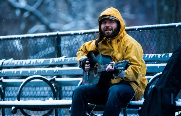 Musician sitting on a park bench busking for tips in New York city