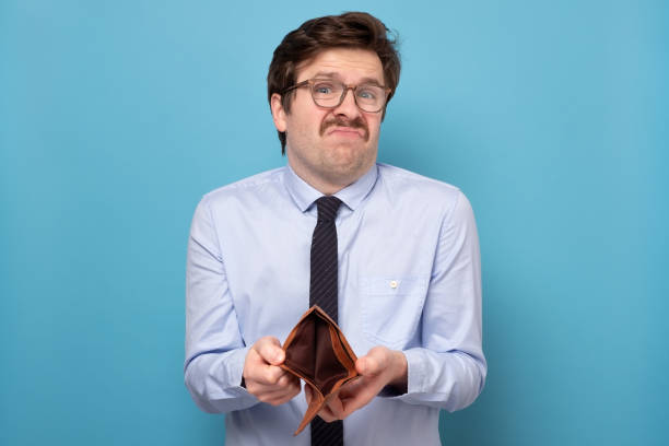 Sad businessman holding an empty wallet isolated on a blue background. stock photo