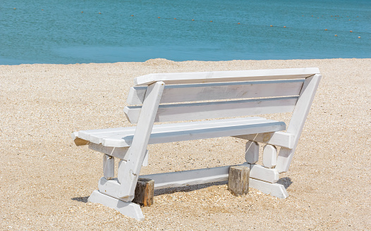 White wooden bench on the sand on a deserted beach, close-up