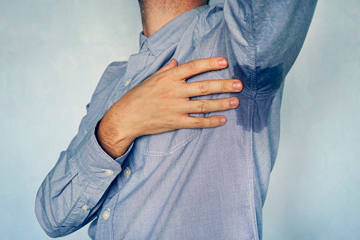 Man with hyperhidrosis sweating very badly under armpit in blue shirt. wet spot on my shirt from sweat.