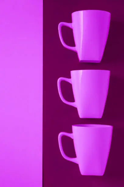 3 pink winter coffee cup mugs lined up in a row for a break time meeting; Copyspace with empty room space for copy text on purple vertical background; Girlie female theme.