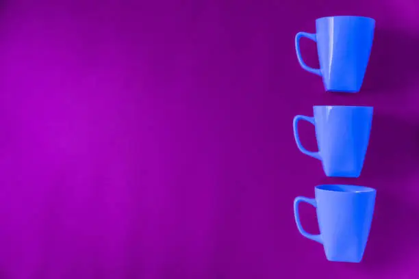 3 blue winter coffee cup mugs lined up in a row for a break time meeting; Copyspace with empty room space for copy text on purple horizontal background