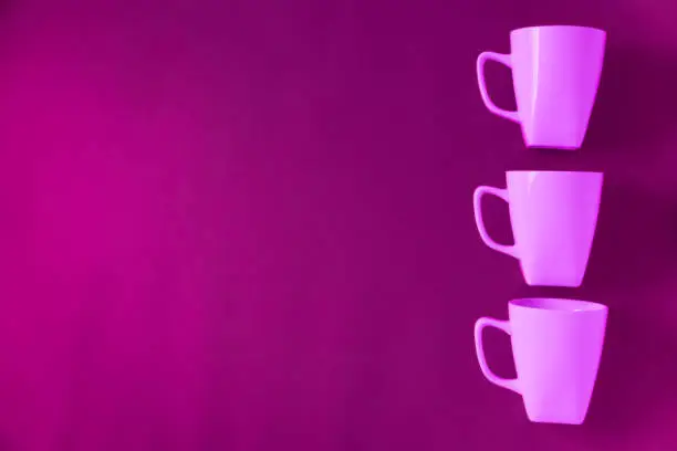 3 pink winter coffee cup mugs lined up in a row for a break time meeting; Copyspace with empty room space for copy text on purple horizontal background; Girlie female theme.