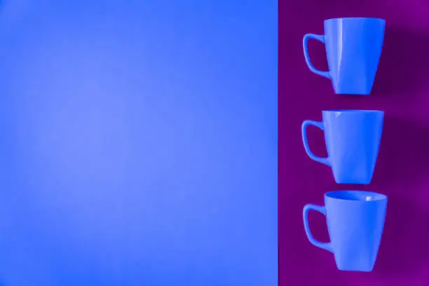 3 blue winter coffee cup mugs lined up in a row for a break time meeting; Copyspace with empty room space for copy text on purple horizontal background