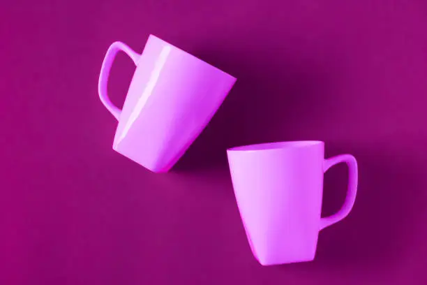 2 isolated pink winter coffee cup mugs for a break time meeting; Copyspace with empty room space for copy text on purple horizontal background; Girlie female theme