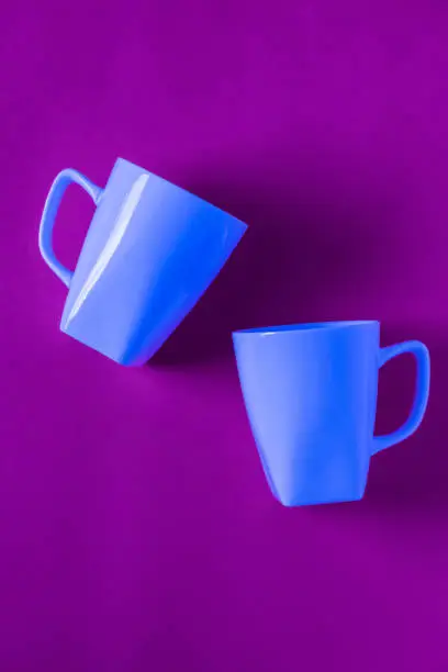 2 isolated blue winter coffee cup mugs for a break time meeting; Copyspace with empty room space for copy text on purple vertical background;