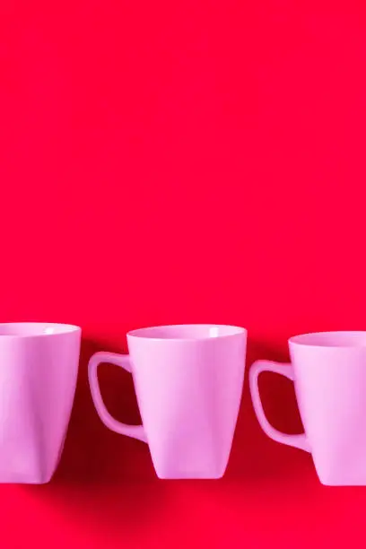 3 pink winter coffee cup mugs lined up in a row for a break time meeting; Copyspace with empty room space for copy text on red vertical background; Girlie female valentines theme.