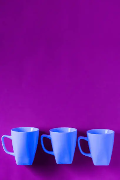 3 blue winter coffee cup mugs lined up in a row for a break time meeting; Copyspace with empty room space for copy text on purple vertical background