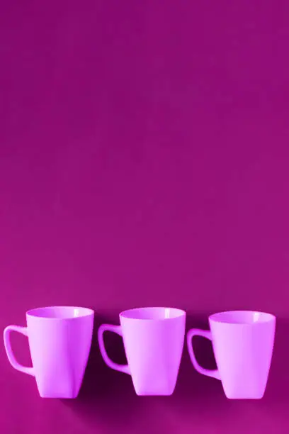 3 pink winter coffee cup mugs lined up in a row for a break time meeting; Copyspace with empty room space for copy text on purple vertical background; Girlie female theme.