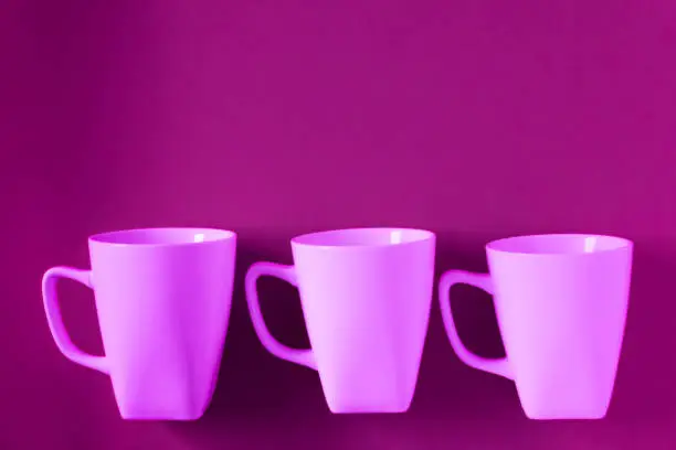3 pink winter coffee cup mugs lined up in a row for a break time meeting; Copyspace with empty room space for copy text on purple horizontal background; Girlie female theme.