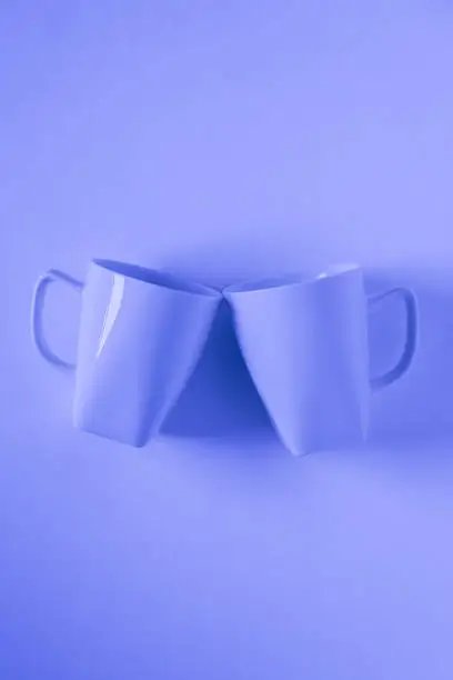 2 monochromatic blue coffee mugs on blue background clinking in cheers with blank empty room space for text, copy, or copyspace. Modern top view concept of two cups with solid background backdrop.