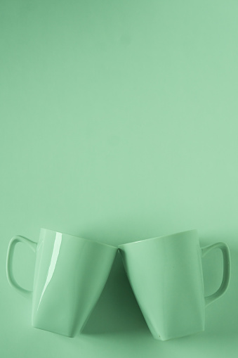 2 monochromatic green coffee mugs on green background clinking in cheers with blank empty room space for text, copy, or copyspace. Modern top view concept of two cups with solid background backdrop.