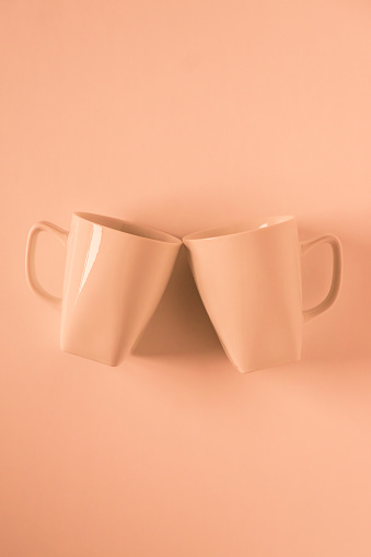 2 monochromatic orange coffee mugs on orange background clinking in cheers with blank empty room space for text, copy, or copyspace. Modern top view concept of two cups with solid background backdrop.