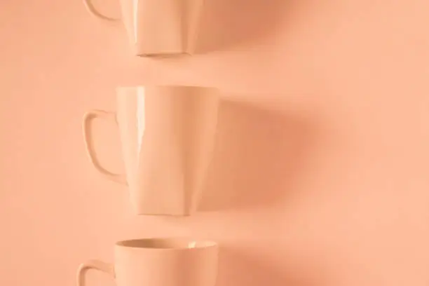 One singled out monochromatic orange coffee mug lined up in a row on orange background with blank empty room space for text, copy, or copyspace. Modern top view concept with solid background backdrop
