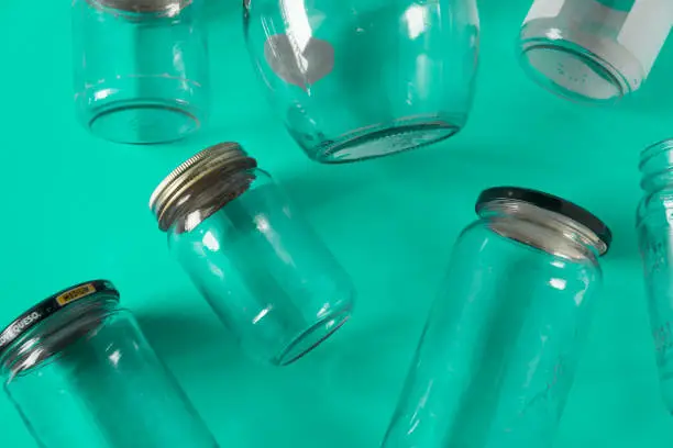 Transparent glass jars with lids isolated on teal green background, top view flat lay recycling concept for environmental awareness. Segregated recyclables mock up conceptual idea, junk waste disposal
