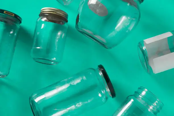 Transparent glass jars with lids isolated on teal green background, top view flat lay recycling concept for environmental awareness. Segregated recyclables mock up conceptual idea, junk waste disposal