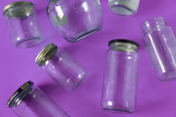 Transparent glass jars with lids isolated on purple background, top view flat lay recycling concept for environmental awareness. Segregated recyclables mock up conceptual idea, junk waste disposal