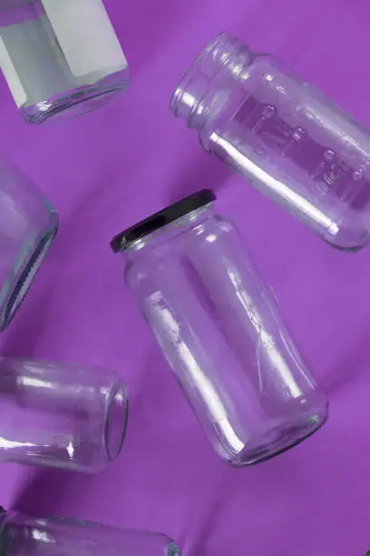 Transparent glass jars with lids isolated on purple background, top view flat lay recycling concept for environmental awareness. Segregated recyclables mock up conceptual idea, junk waste disposal