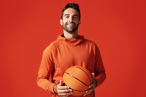 Studio shot of a handsome young man playing basketball against a red background