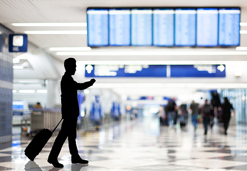 Silhouette of businessman with suitcase checking time while waiting for flight