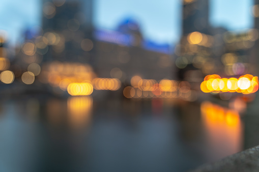 An out of focus skyline background photo of buildings along the Chicago River in downtown at night with the street lights creating round bokeh balls and reflections in the water.